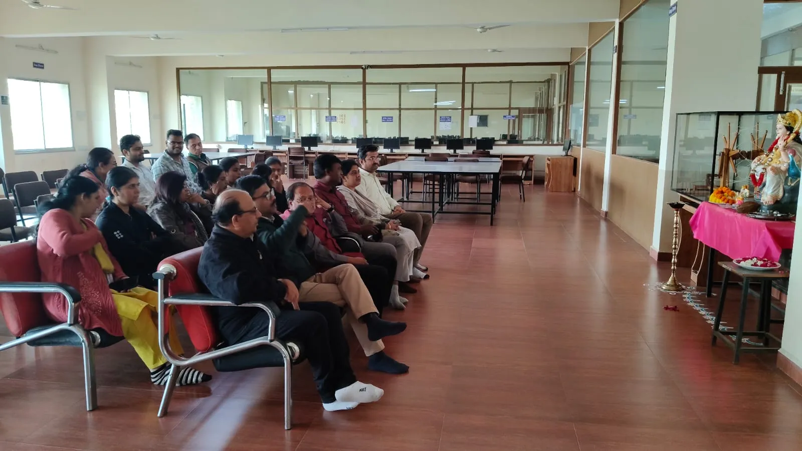 Faculty and staff members seated in the college library hall attending the Vasant Panchami Saraswati Puja celebration
